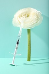 Photo of Cosmetology. Medical syringe and ranunculus flower on turquoise background