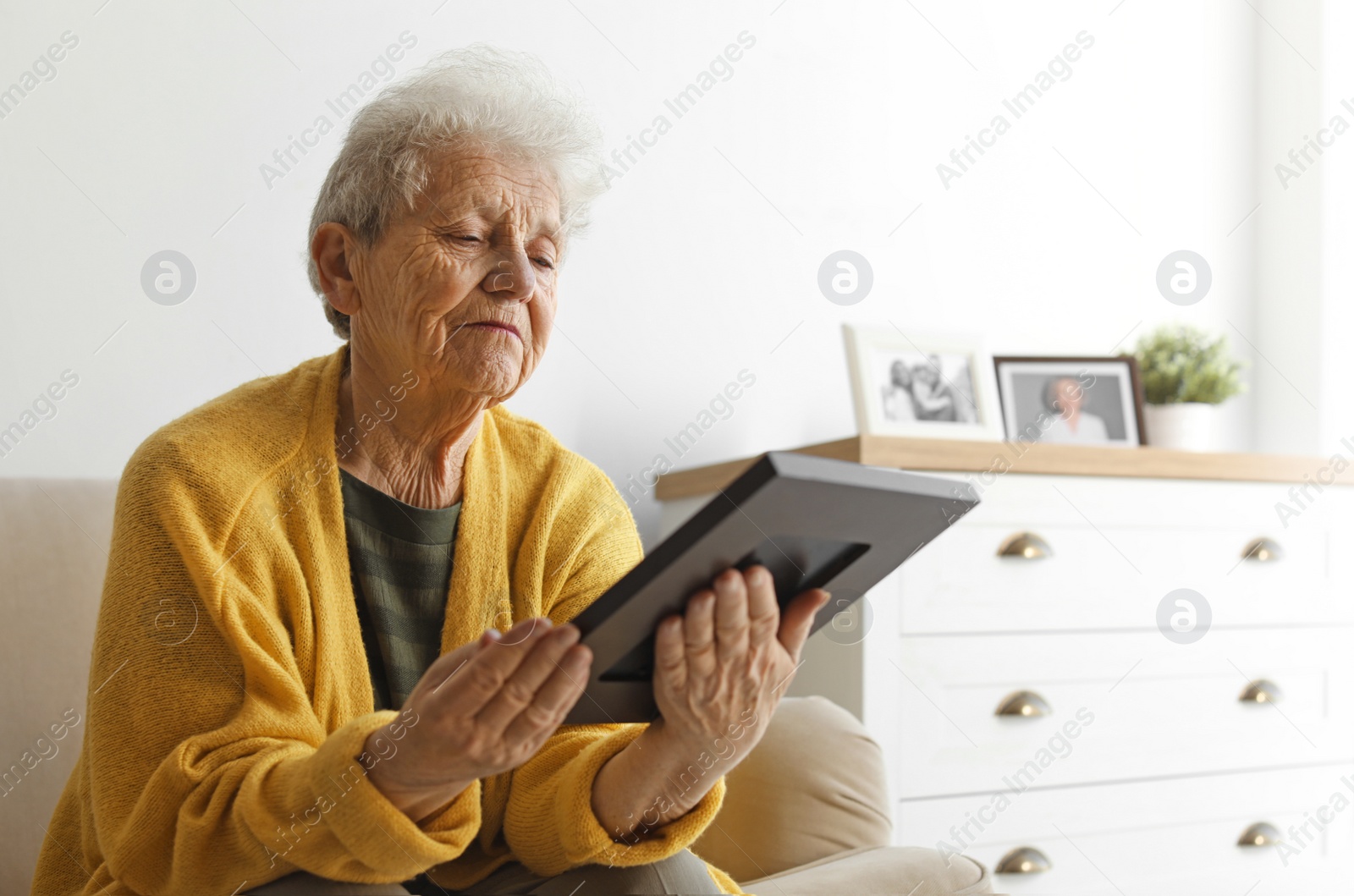 Photo of Elderly woman with framed photo on sofa at home