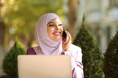 Muslim woman talking on phone in outdoor cafe