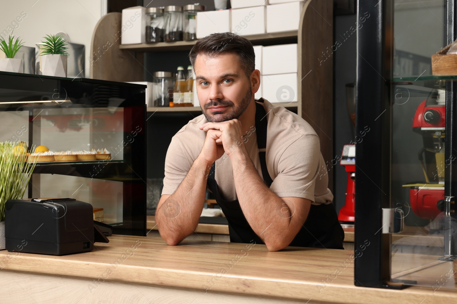 Photo of Business owner near showcases with pastries in his cafe