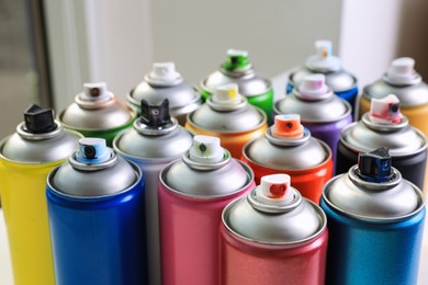 Cans of different graffiti spray paints on blurred background, closeup