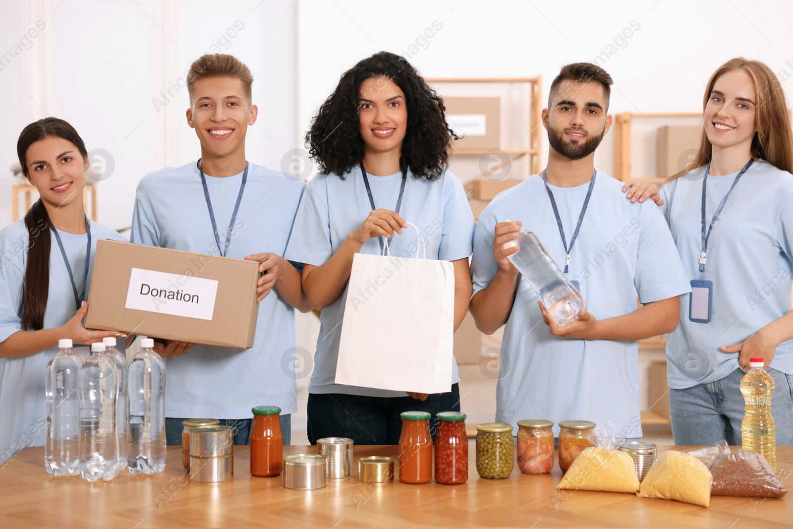 Photo of Portrait of volunteers with donation box, paper bag and food products at table in warehouse