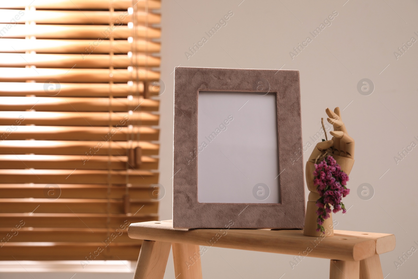 Photo of Empty photo frame and decorative hand with flowers on wooden table indoors, space for text