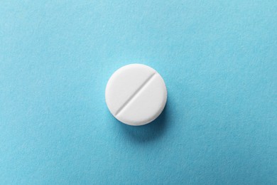 Photo of One white pill on light blue background, top view