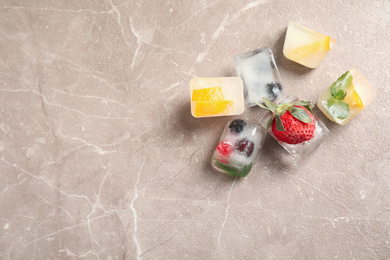 Photo of Ice cubes with different berries and mint on grey table, flat lay. Space for text