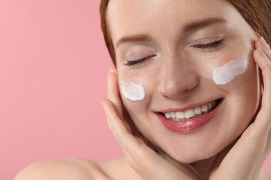 Smiling woman with freckles and cream on her face against pink background, closeup. Space for text