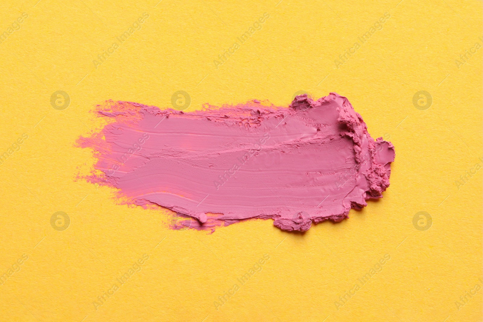 Photo of Smear of bright lipstick on yellow background, top view