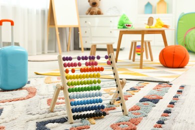 Photo of Colorful toy abacus on rug in playroom. Kindergarten interior design