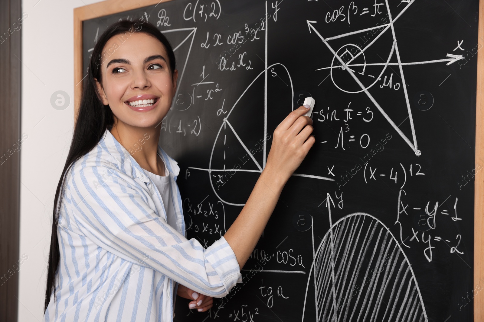 Photo of Happy teacher explaining mathematics at chalkboard in classroom