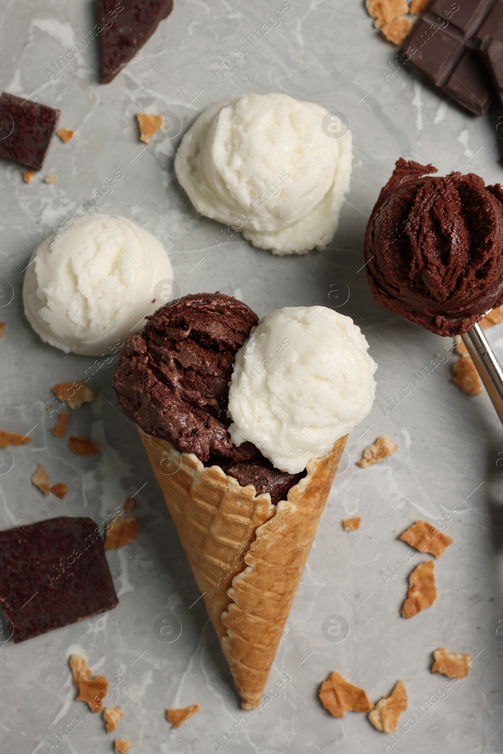 Photo of Flat lay composition with tasty ice cream scoops, pieces of chocolate and waffle cone on light marble table