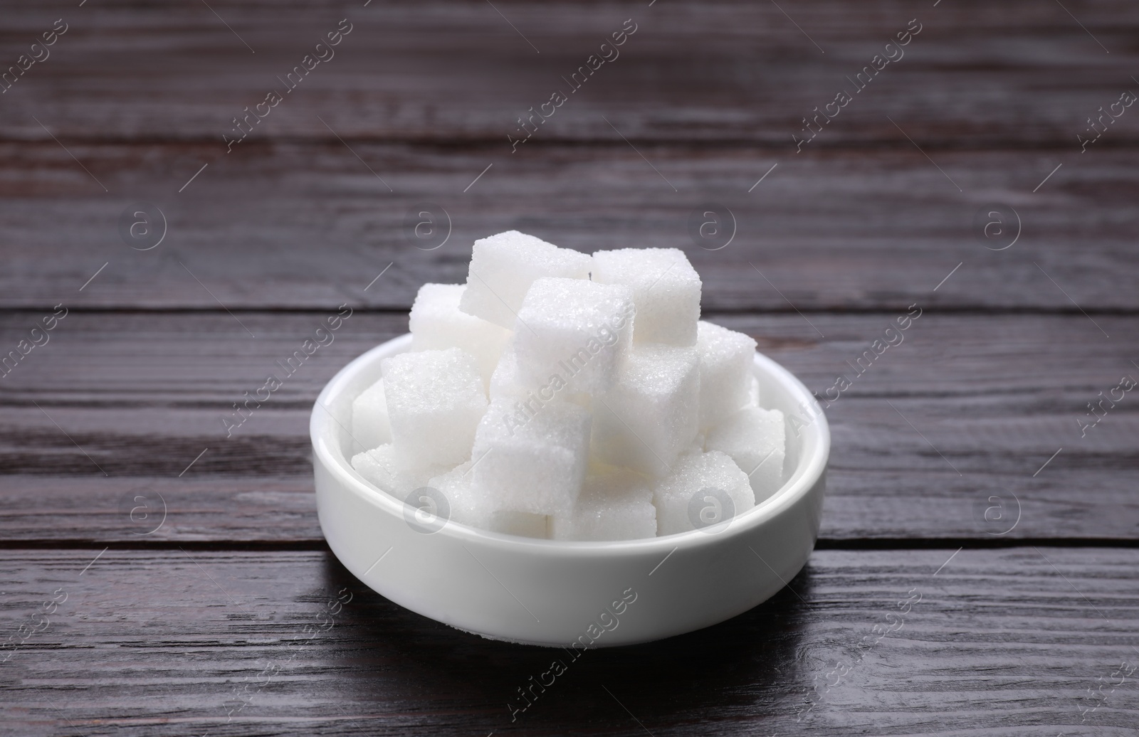 Photo of White sugar cubes in bowl on wooden table