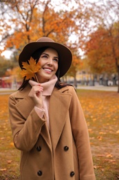 Photo of Young woman in stylish clothes holding yellow leaf outdoors. Autumn look