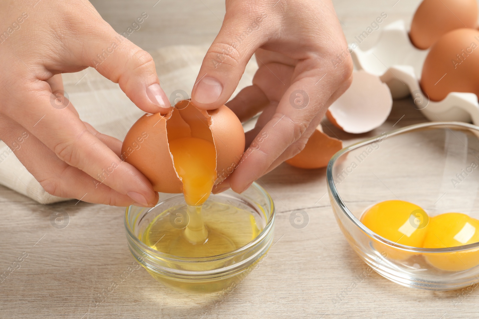 Photo of Woman separating egg yolk from white over glass bowl at wooden table, closeup