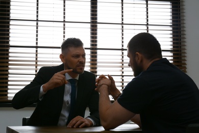Photo of Angry detective interviewing criminal in interrogation room