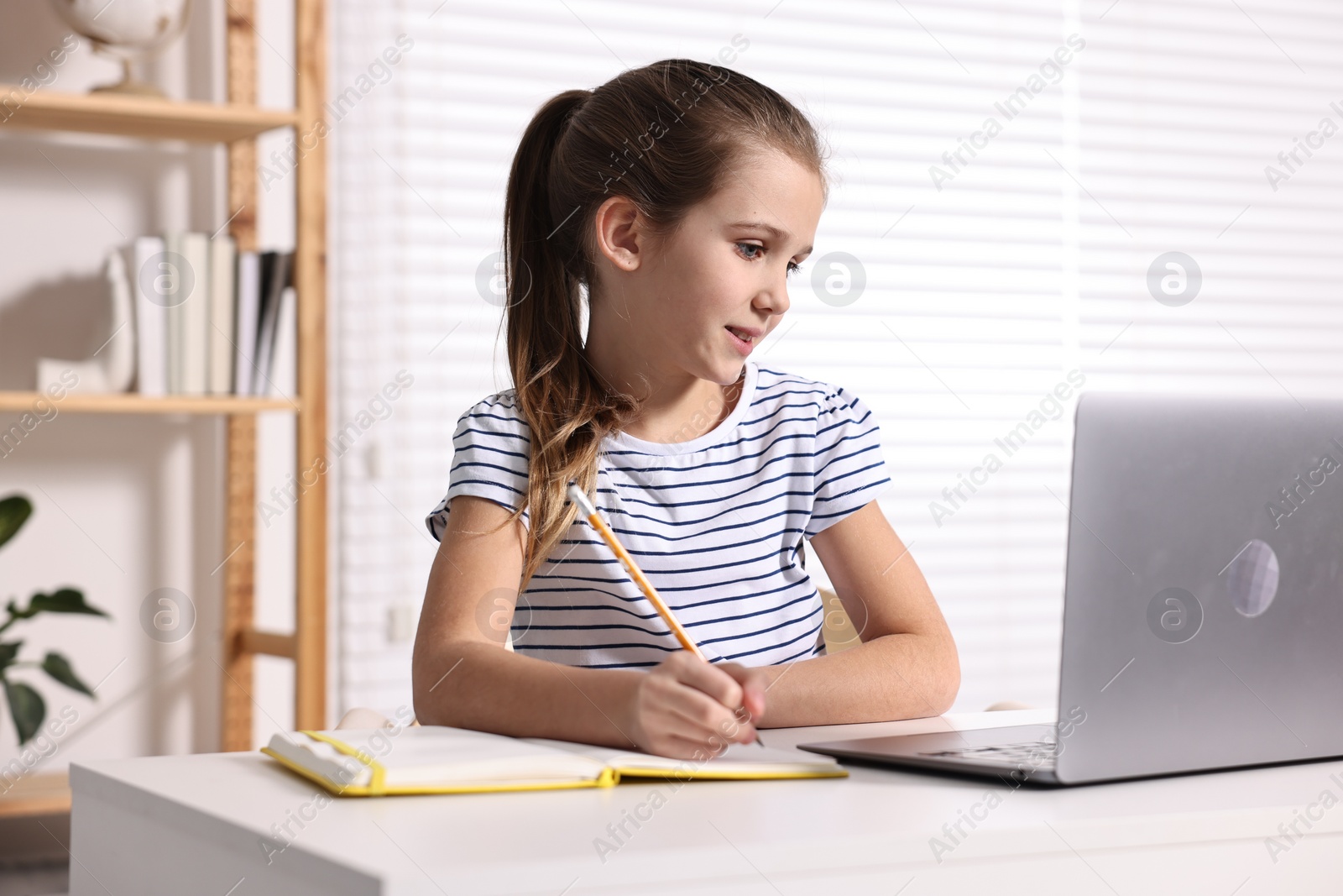 Photo of E-learning. Cute girl taking notes during online lesson at table indoors