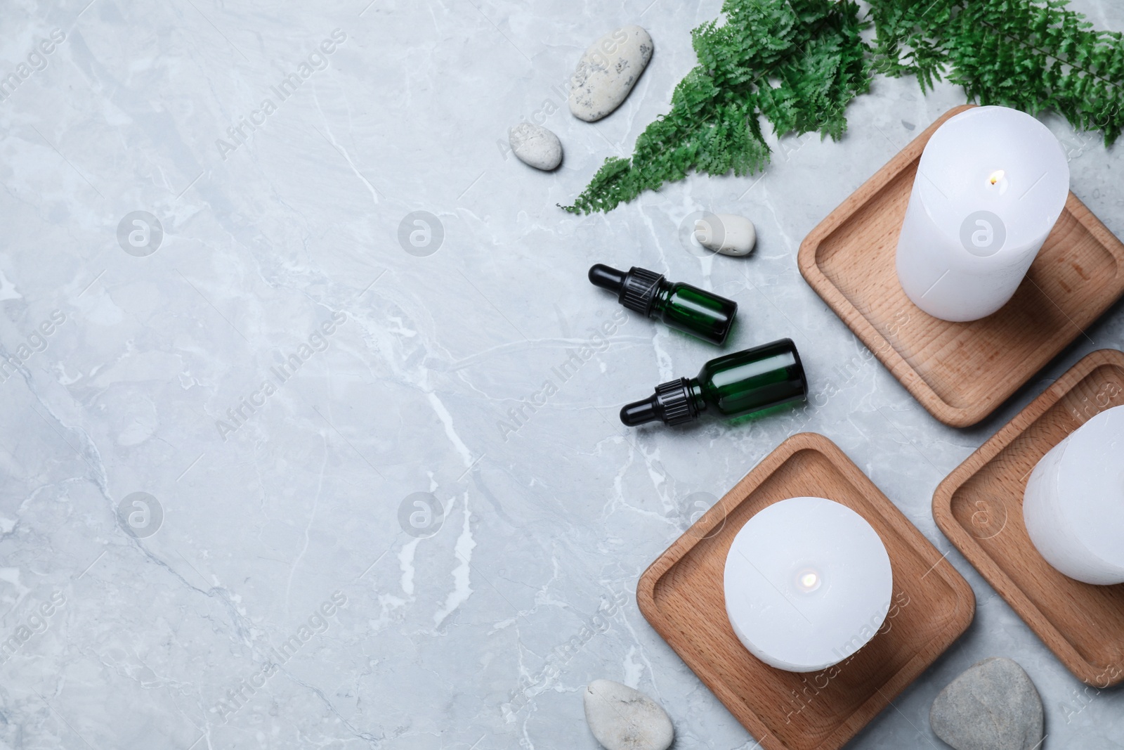 Photo of Burning candles, stones and essential oil on grey marble table, flat lay. Space for text