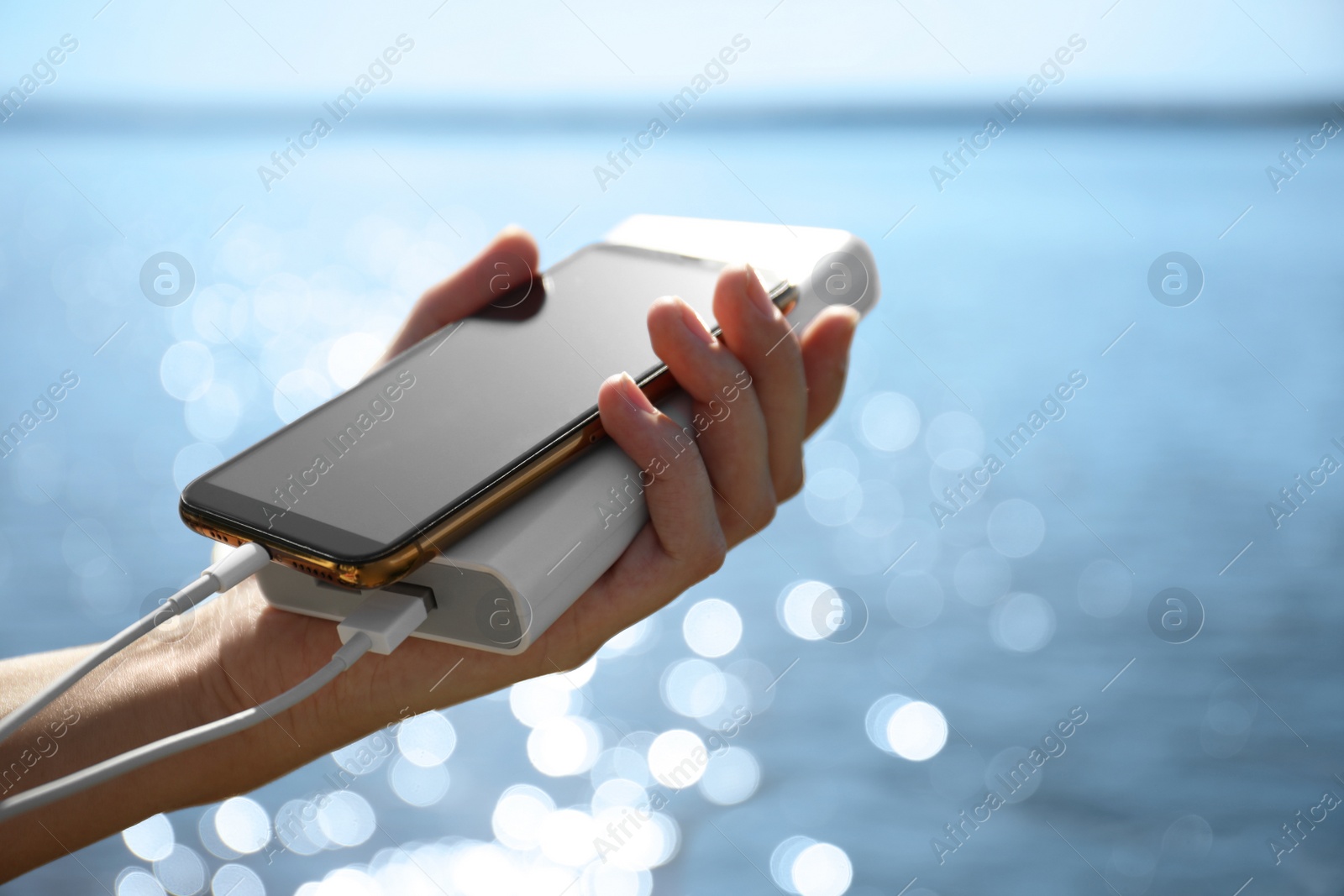 Photo of Woman charging smartphone with power bank on rocky mountain near river, closeup