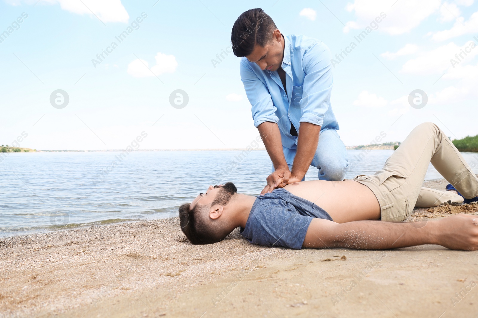 Photo of Passerby performing CPR on unconscious young man near sea. First aid