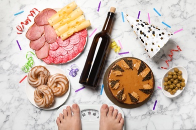 Woman using scale surrounded by food and alcohol after party on floor, top view. Overweight problem