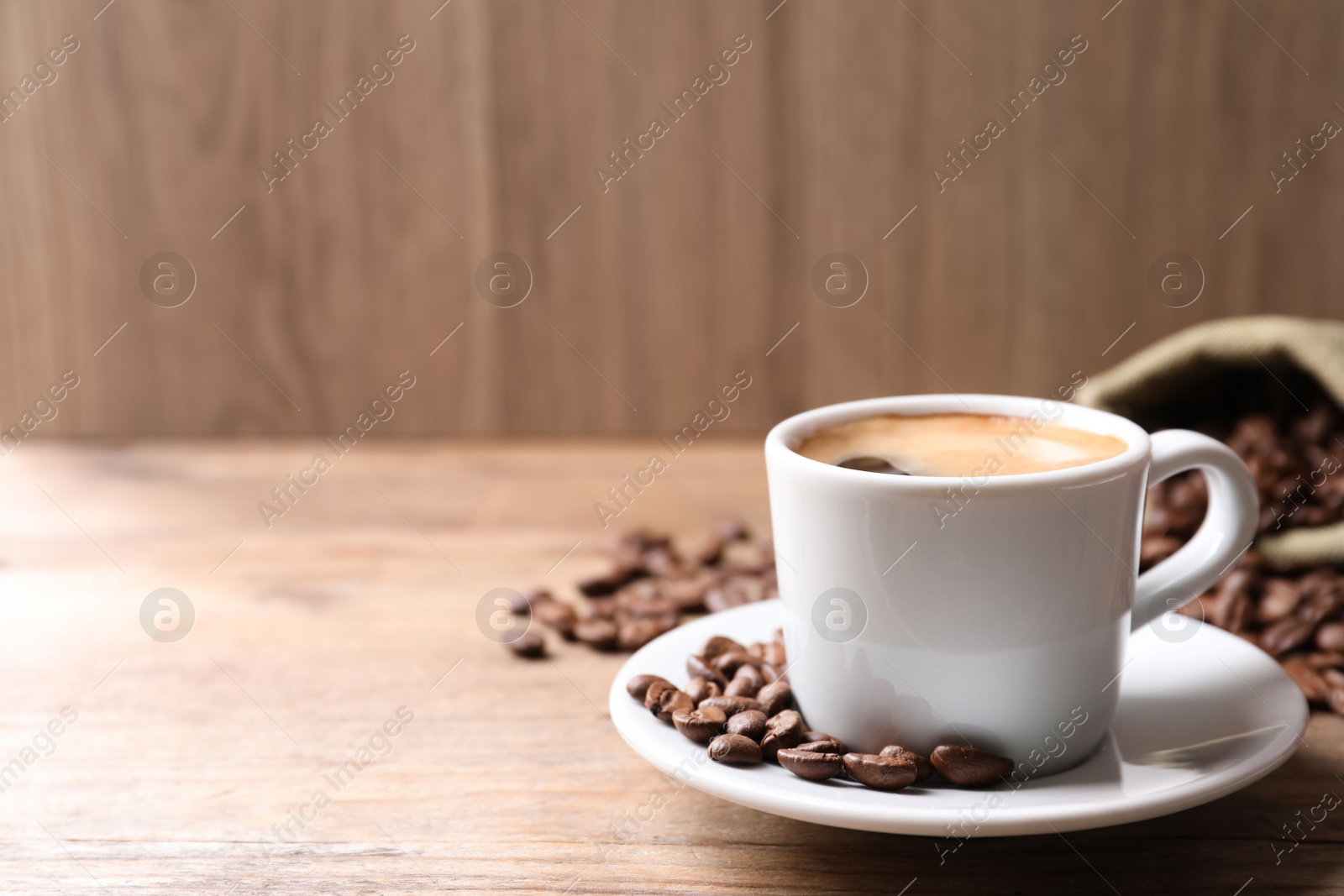 Photo of Cup of hot aromatic coffee and roasted beans on wooden table. Space for text