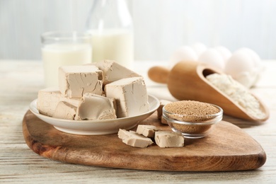 Compressed and granulated yeast on white wooden table