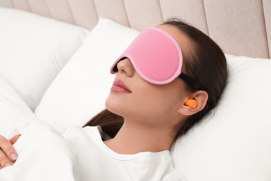 Photo of Young woman with foam ear plugs and mask sleeping in bed
