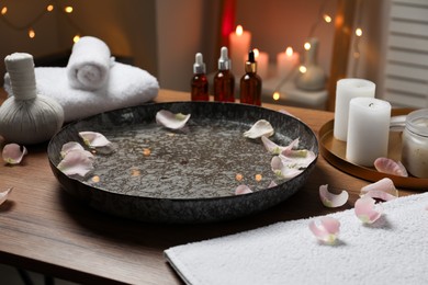 Photo of Bowl of water with flower petals on wooden table in spa