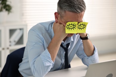 Man with fake eyes painted on sticky notes snoozing at workplace in office