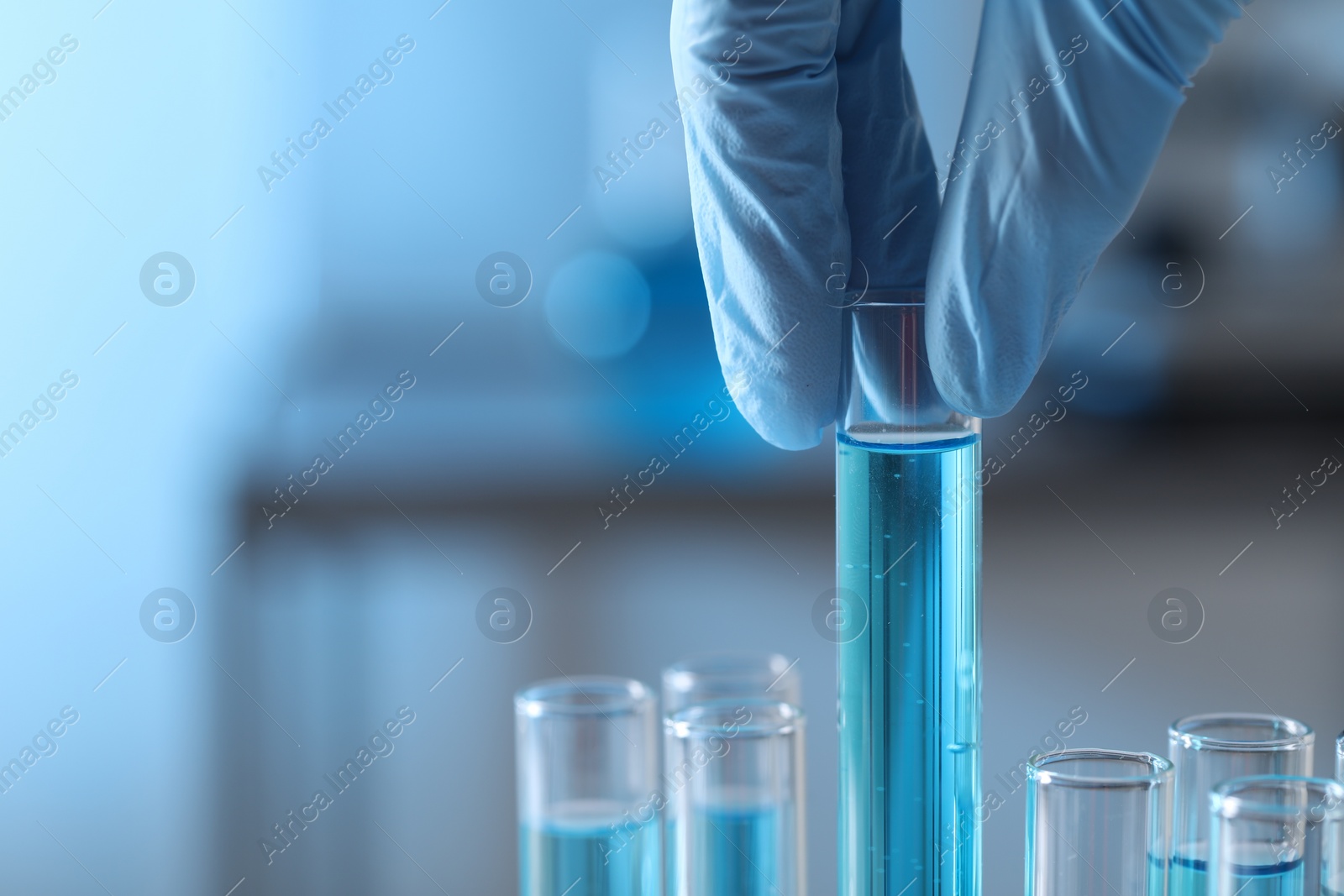 Photo of Scientist taking test tube with light blue liquid in laboratory, closeup. Space for text