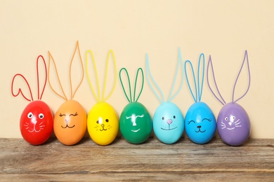 Image of Colorful eggs as Easter bunnies on wooden table against beige background