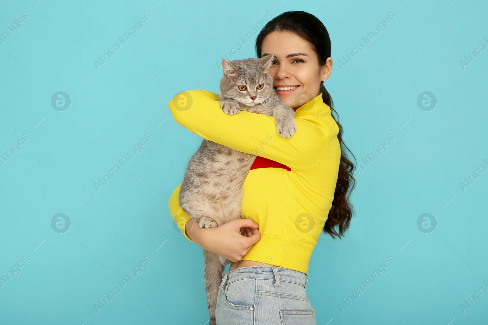 Photo of Young woman with adorable cat on light blue background, space for text