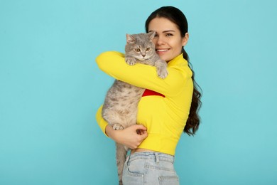 Young woman with adorable cat on light blue background, space for text