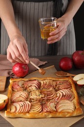 Photo of Woman adding honey to freshly baked apple pie at table, closeup