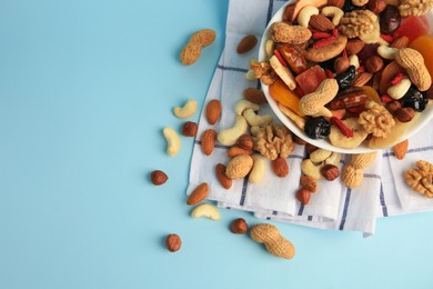 Bowl with mixed dried fruits and nuts on light blue background, above view. Space for text