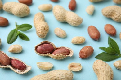 Fresh peanuts and leaves on light blue table, above view