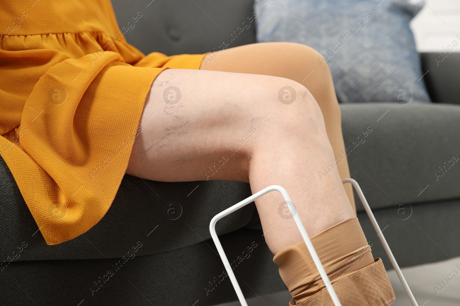 Photo of Woman putting on compression tights with stocking donner in living room, closeup. Prevention of varicose veins