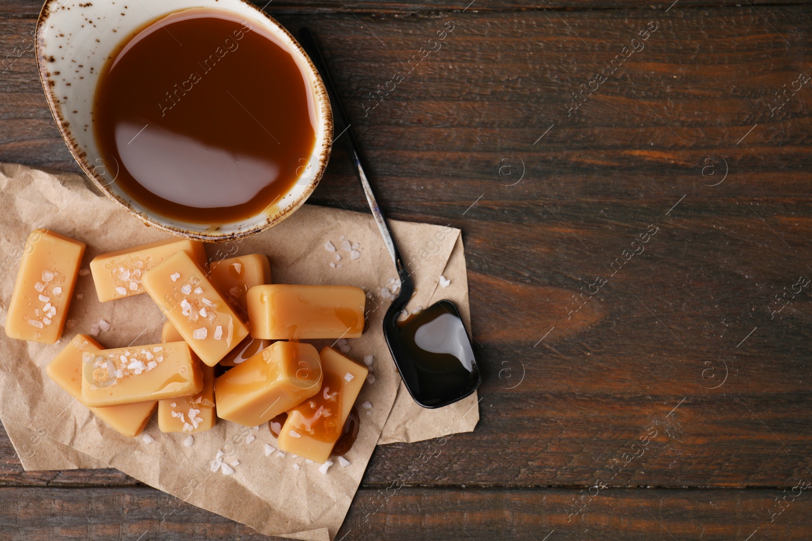 Photo of Delicious candies with sea salt and caramel sauce on wooden table, flat lay. Space for text