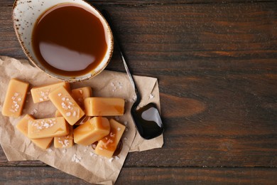 Delicious candies with sea salt and caramel sauce on wooden table, flat lay. Space for text