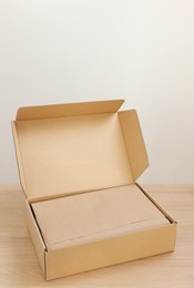 Photo of Open cardboard box with item wrapped in kraft paper on wooden table. Delivery service