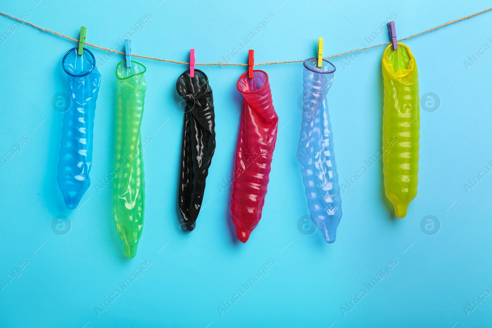 Photo of Used colorful condoms hanging on clothesline against light blue background. Safe sex concept