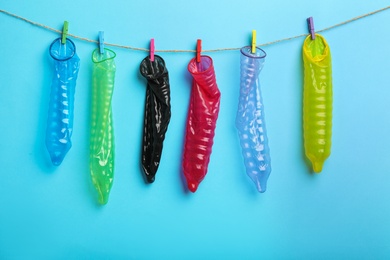 Used colorful condoms hanging on clothesline against light blue background. Safe sex concept