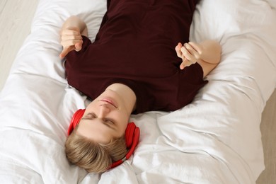 Photo of Teenage boy listening to music with headphones on bed, above view