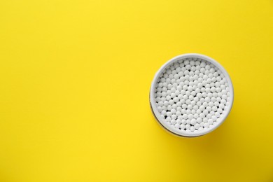 Photo of Container with new cotton buds on yellow background, top view. Space for text