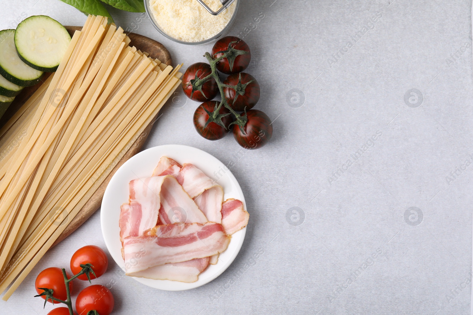 Photo of Raw pasta and fresh ingredients on light grey table, flat lay. Space for text