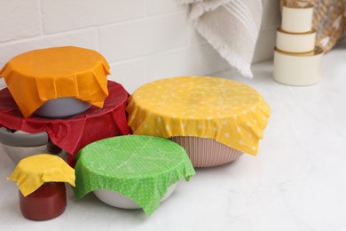 Photo of Different dishware covered with beeswax food wraps on white marble table. Space for text