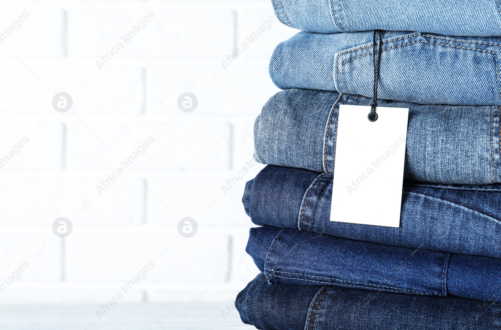Photo of Stack of different jeans near white brick wall, closeup. Space for text