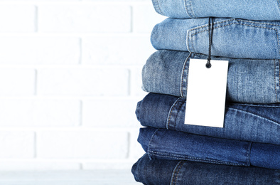 Photo of Stack of different jeans near white brick wall, closeup. Space for text