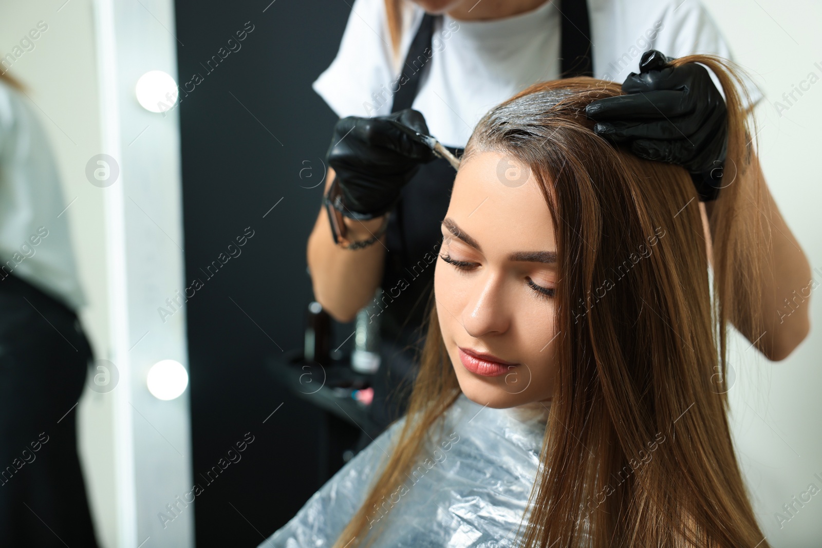 Photo of Professional hairdresser dyeing client's hair in beauty salon