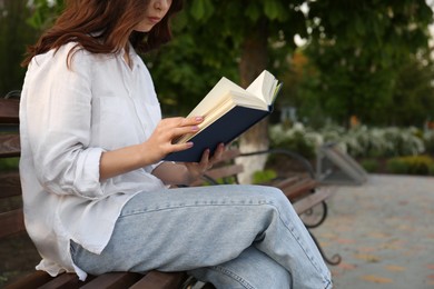 Photo of Young woman reading on bench in park, closeup