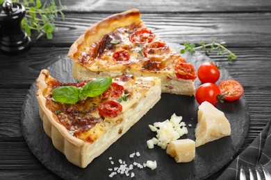 Pieces of delicious homemade quiche with prosciutto and ingredients on black wooden table, closeup